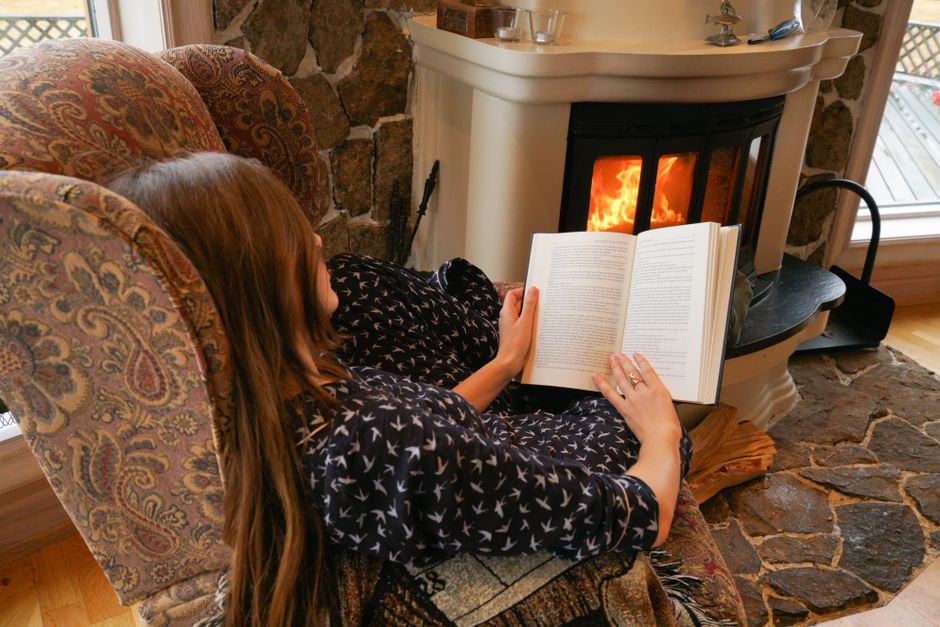 Personne lisant un livre au coin d'un poêle allumé, ambiance chaleureuse
